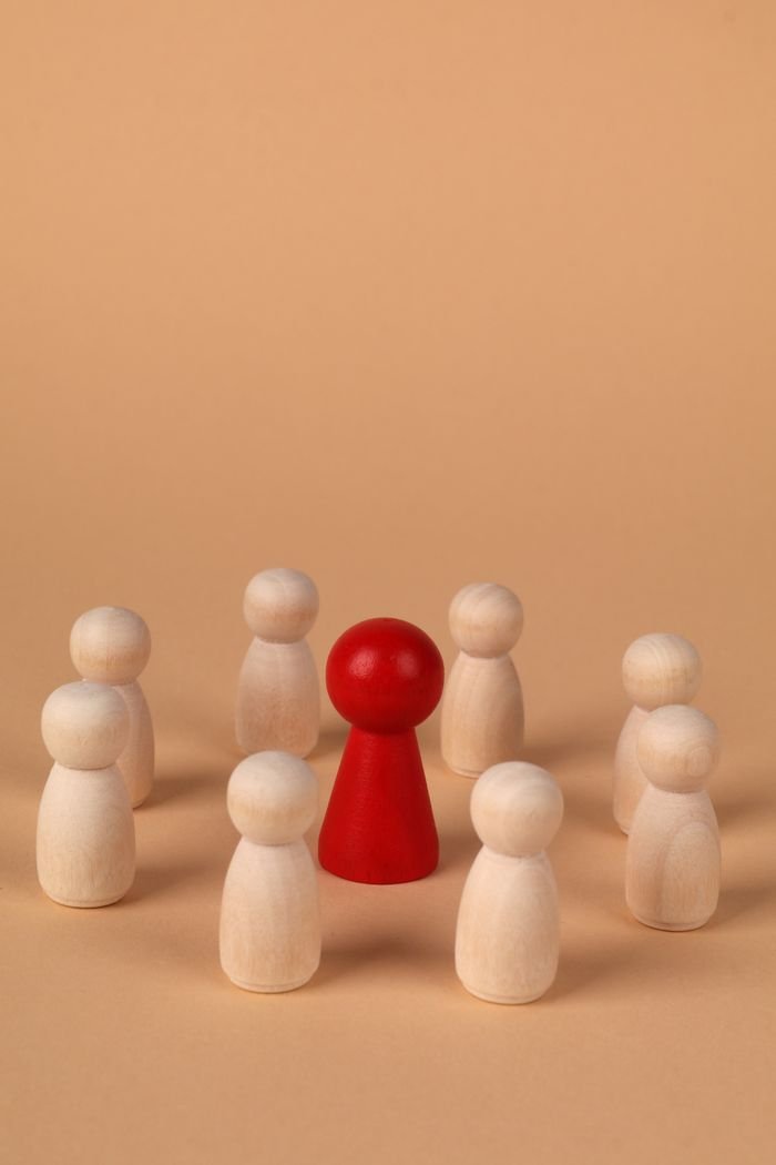 A red wooden figure stands out among natural wooden figures, symbolizing leadership and individuality.