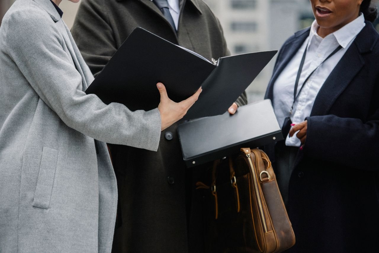 Crop diverse coworkers wearing formal outfits reading documents together and discussing project on street